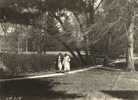 Two students walk on campus, ca. 1920