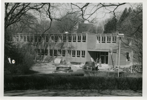Three men standing by a building under construction, undated