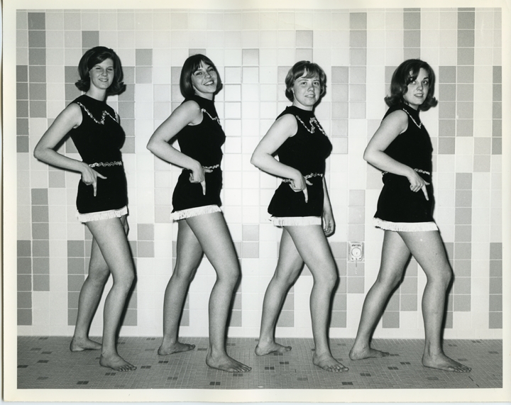 Four team members posing in black one-piece swimsuits