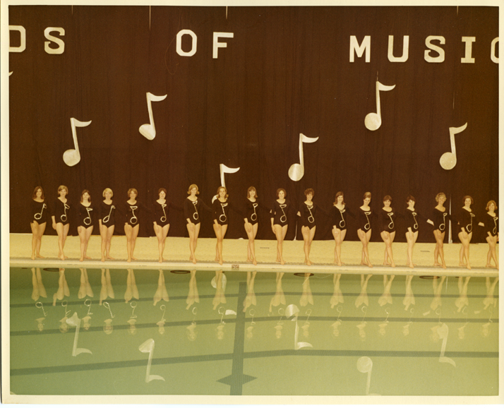 Eighteen women in black one-pieces standing by the pool
