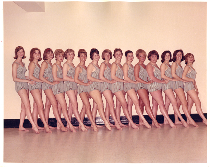 15 women posing in a line in striped swimsuits